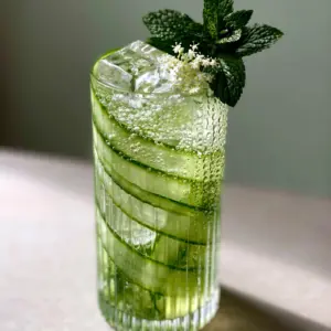 Close up of a Cucumber Spritz showing carbonation bubbles trapped against coiled cucumber ribbons and square clear ice.